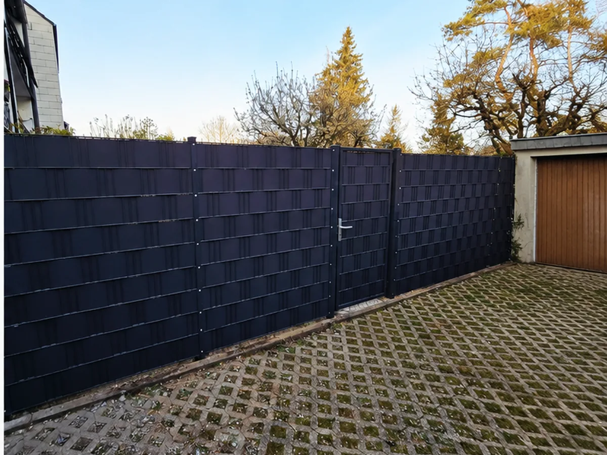 Doppelstabmattenzaun mit Sichtschutzstreifen und Gartentür an einer Einfahrt mit Rasengittersteinen